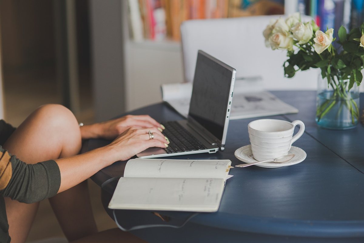Une personne travaille sur ordinateur portable à une table avec cahier, tasse et fleurs Une personne travaille sur ordinateur portable à une table avec cahier, tasse et fleurs
