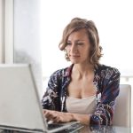 Une femme utilise un ordinateur portable près d'une grande fenêtre