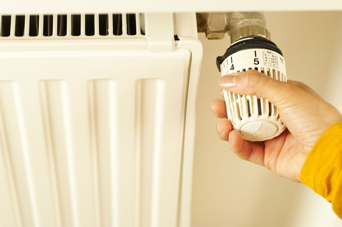 Une main ajuste le thermostat d'un radiateur blanc Une main ajuste le thermostat d'un radiateur blanc